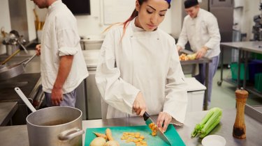 Eine junge Frau, ein Lehrling, schneidet unglücklich Gemüse in einer Großküche