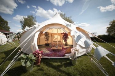 Bauchiges weißes Glamping-Zelt von Glampingwelt, luxuriös mit Bett, Teppich und Dekoration eingerichtet.