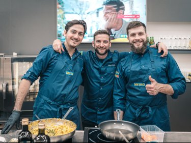 Drei Männer in Kochschürzen stehen Arm in Arm