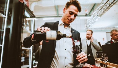 Aussteller auf der "Alles für den Gast" 2021 schenkt sich aus einer Weinflasche Rotwein in ein Weinglas ein.